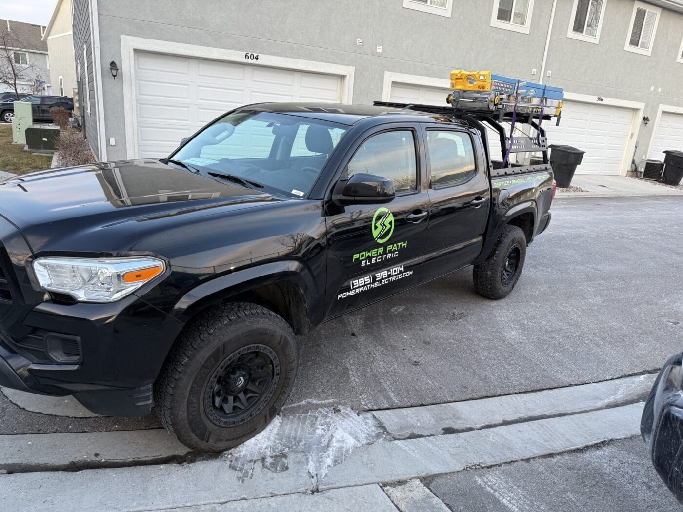 Black pickup truck parked on a residential street with a logo and contact information for 