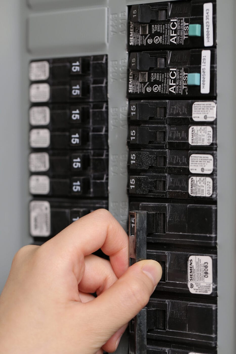 A hand flipping a switch on a circuit breaker panel, with multiple labeled switches visible, showcasing electrical service upgrades in action.