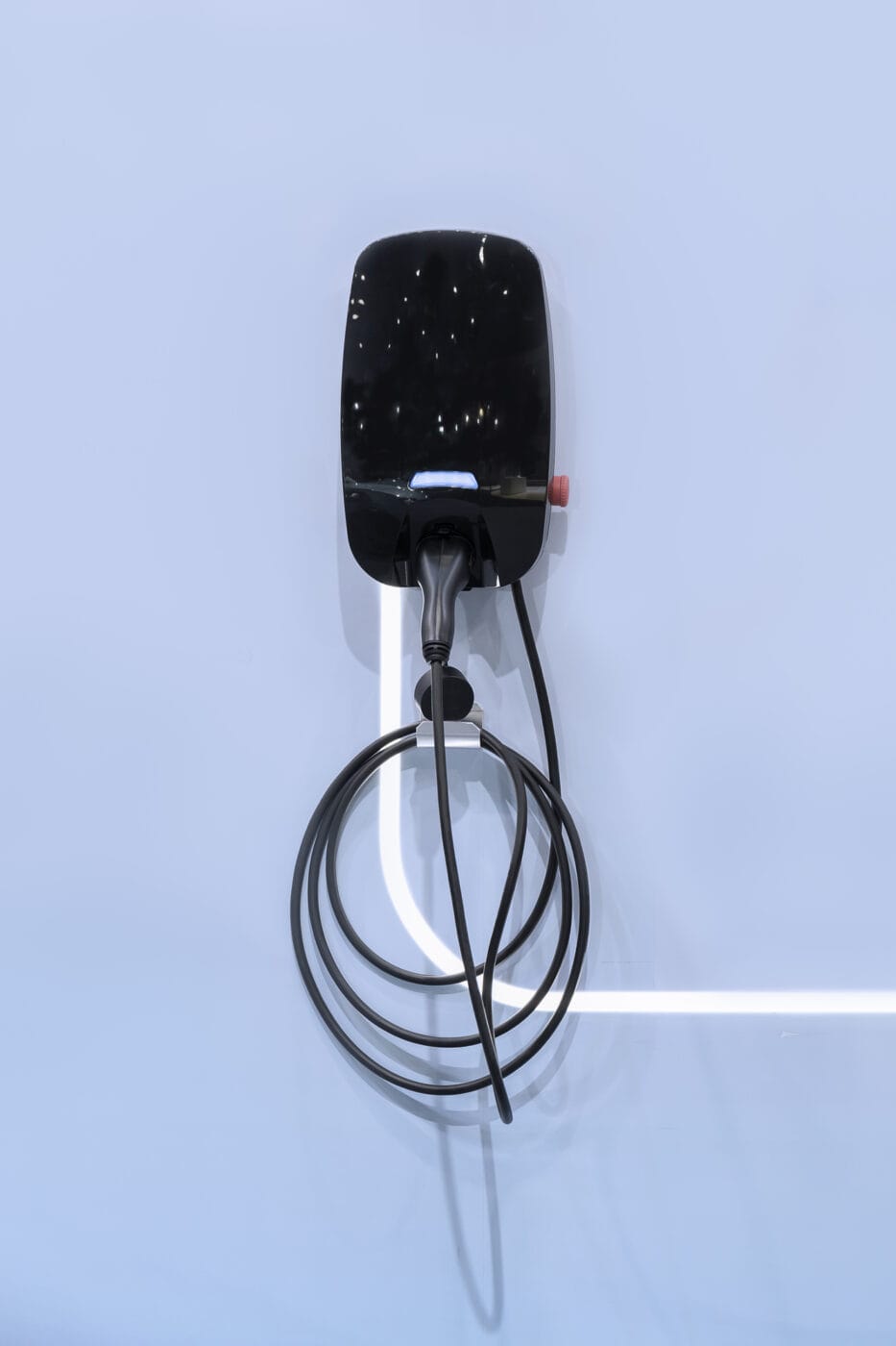 Electric vehicle charging station with coiled cable mounted on a light blue wall.